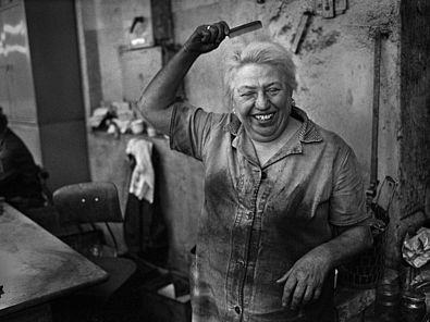 Auf dem Foto ist eine Frau im kohleverschmierten Arbeitskittel zu sehen, die sich lachend die Haare kämmt.