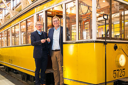 Dr. Rolf Erfurt, Vorstand Betrieb der BVG und Joachim Breuninger, Vorstand der Stiftung Deutsches Technikmuseum, stehen in einem historischen S-Bahn-Wagen, Dr. Rolf Erfurt überreicht symbolisch einen Schlüssel.
