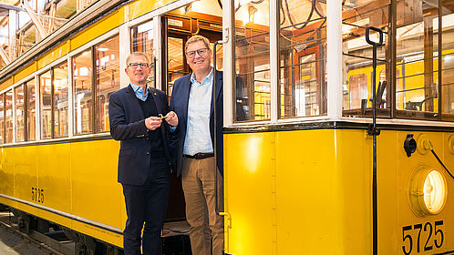 Dr. Rolf Erfurt, Vorstand Betrieb der BVG und Joachim Breuninger, Vorstand der Stiftung Deutsches Technikmuseum, stehen in einem historischen S-Bahn-Wagen, Dr. Rolf Erfurt überreicht symbolisch einen Schlüssel.