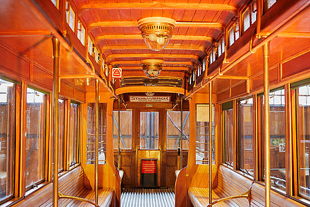 Blick in den Innenraum eines historischen U-Bahnwagens. Die Einrichtung ist aus edlem Holz, die Formen sind geschwungen und elegant, das Design ist dem Jugenstil zuzuordnen.