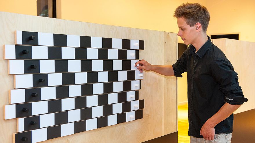 Ein Mann bedient ein Experiment an einer Wand: Schwarz-weiß gestreifte Leisten sind gegeneinander verschoben. Sie erscheinen schief.
