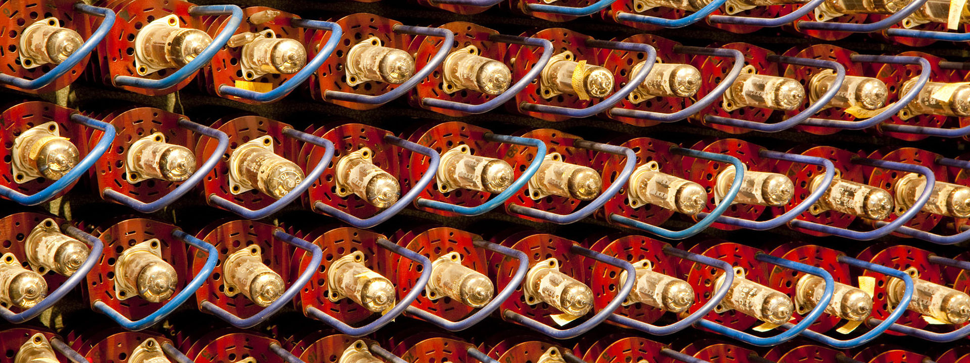 Bildfüllend: rote Elektroröhren mit goldfarbenen Metallkappen und blauen Bügeln