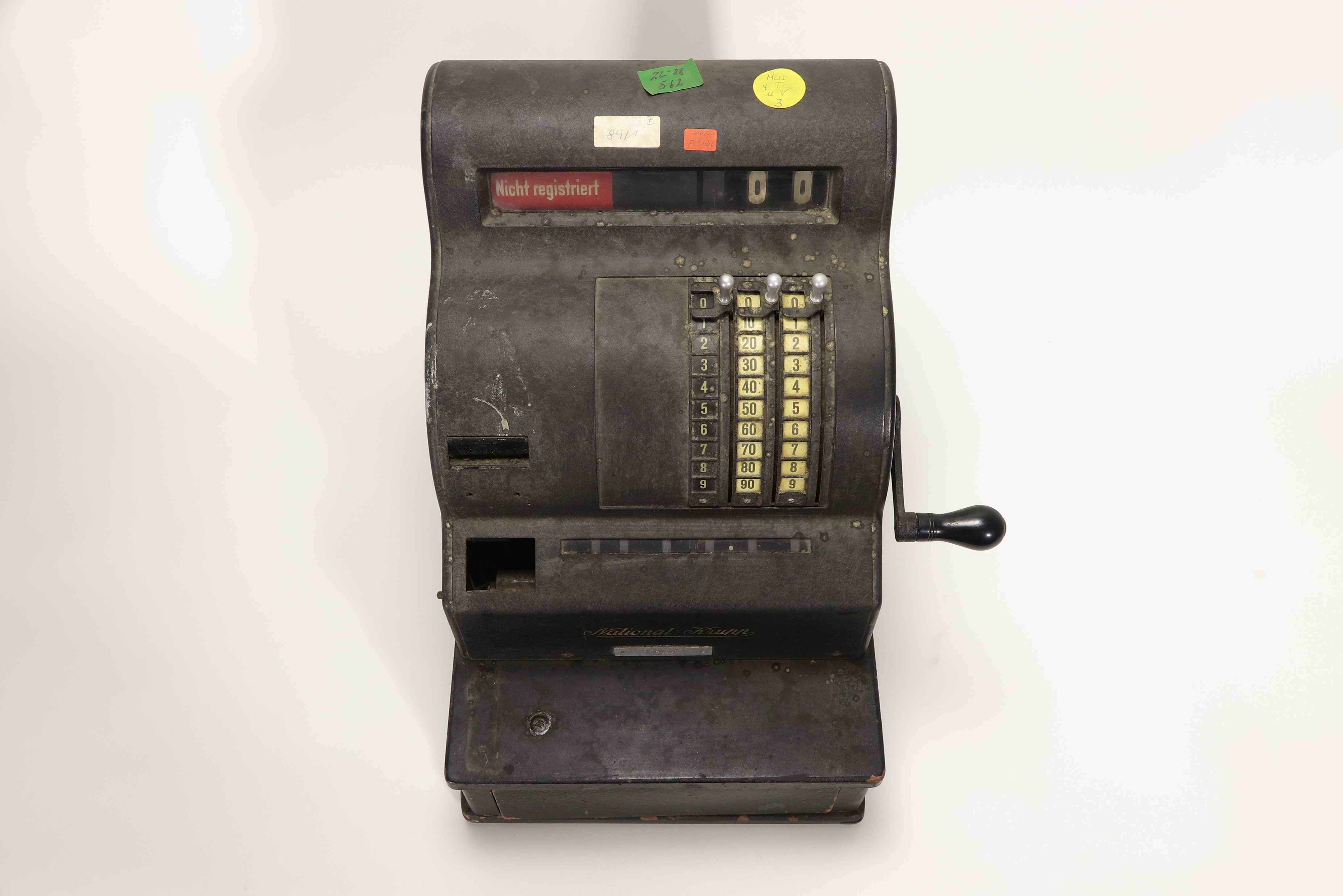 Registrierkasse aus den 1930er Jahren mit vier farbigen Aufklebern der KuA. Die Aufkleber tragen Zahlen und Buchstaben.