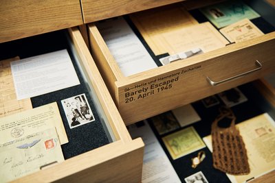 A view inside two open drawers containing documents, letters, and photos. One drawer is labeled: Hella and Hannelore Zacharias. Barely Escaped, April 20, 1945