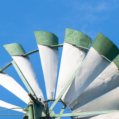 Die obere Hälfte eines Windrads mit grünen Spitzen vor blauem Himmel
