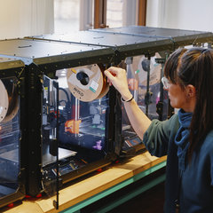 Eine Frau sitzt vor drei 3D-Druckern im TechLab des Deutschen Technikmuseums.