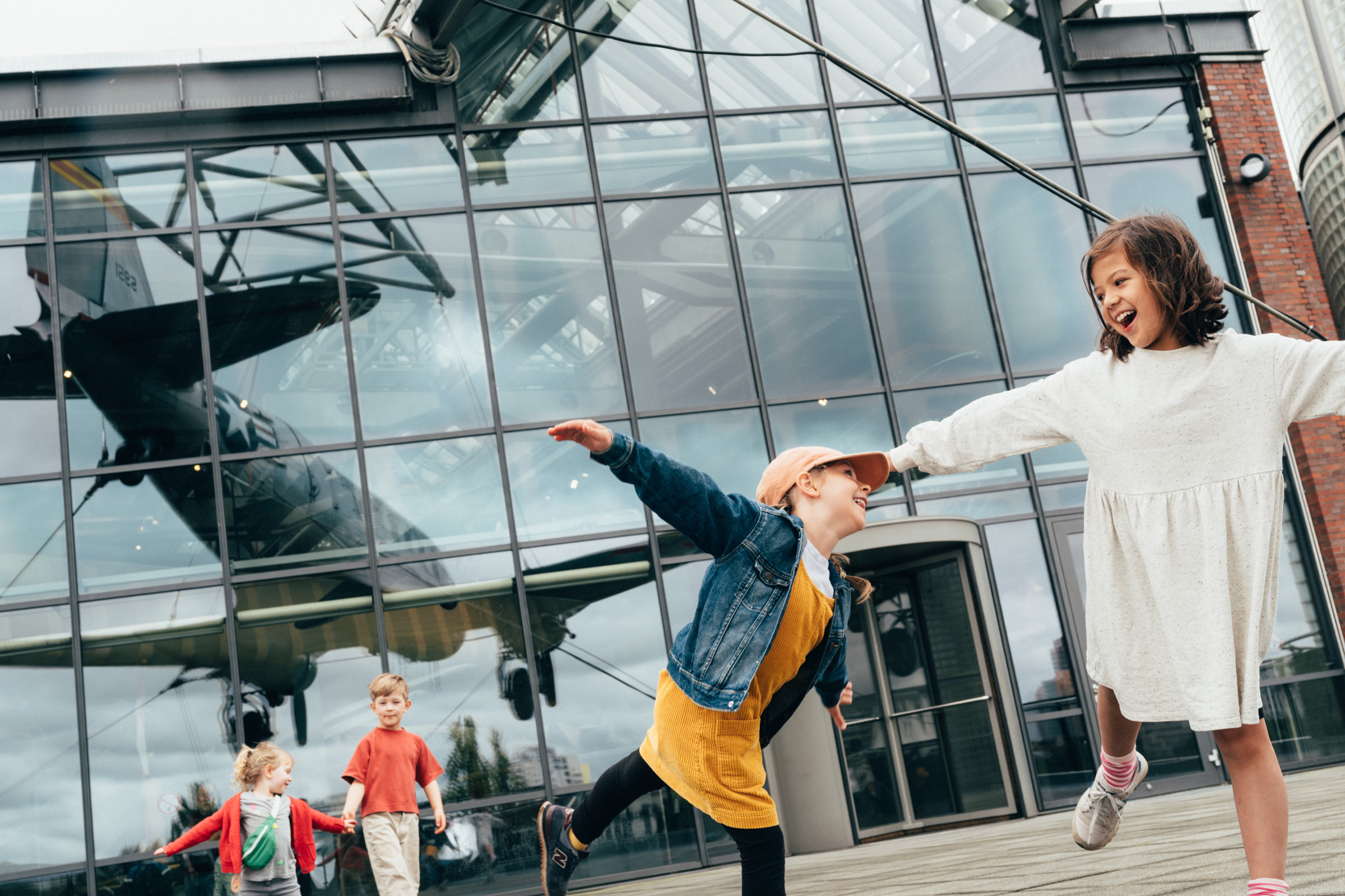 Vier Kinder auf der Terrasse des Deutschen Technikmuseums, in der Glasfront spiegelt sich der Rosinenbomber.