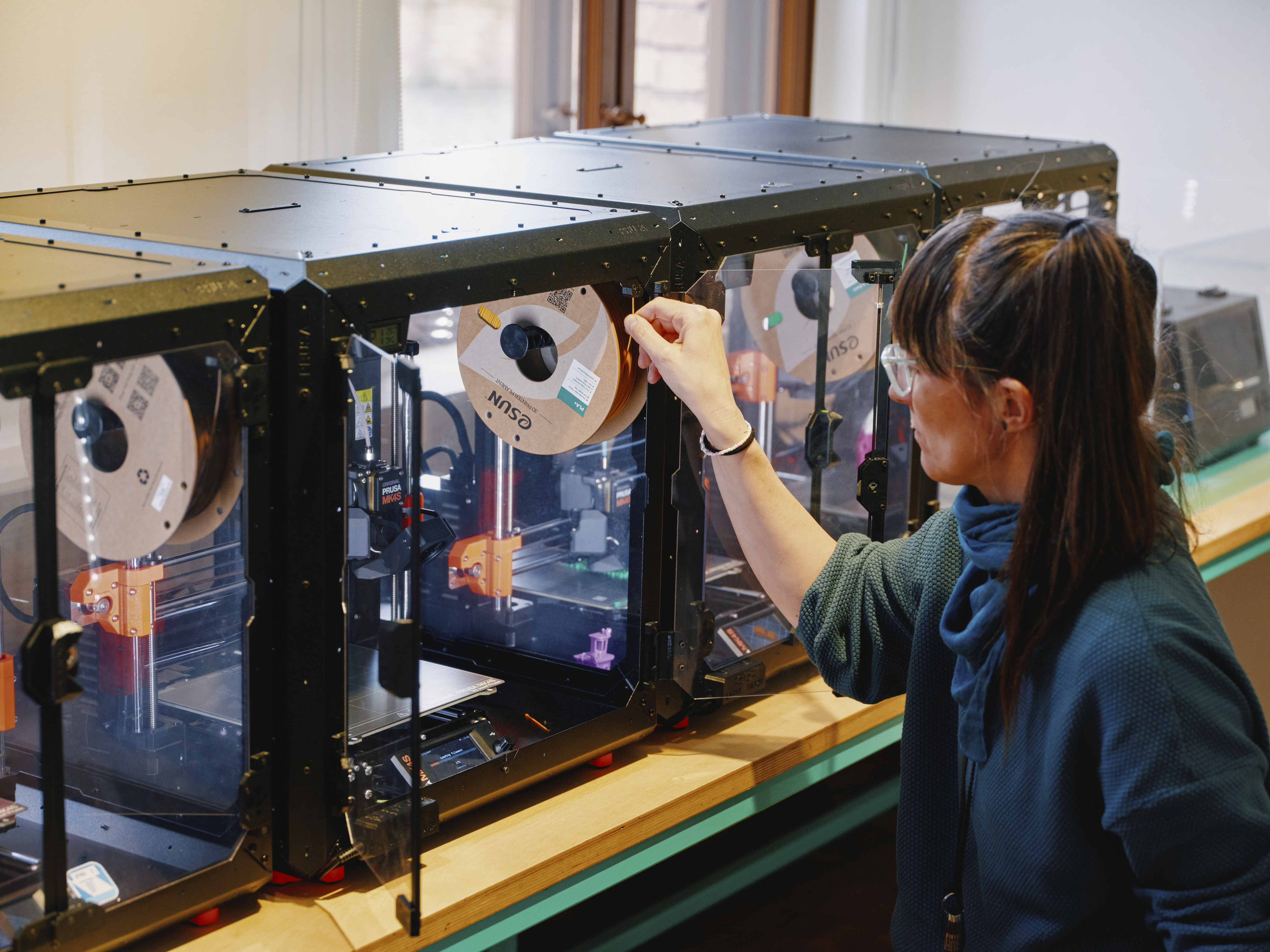 Eine Frau sitzt vor drei 3D-Druckern im TechLab des Deutschen Technikmuseums.