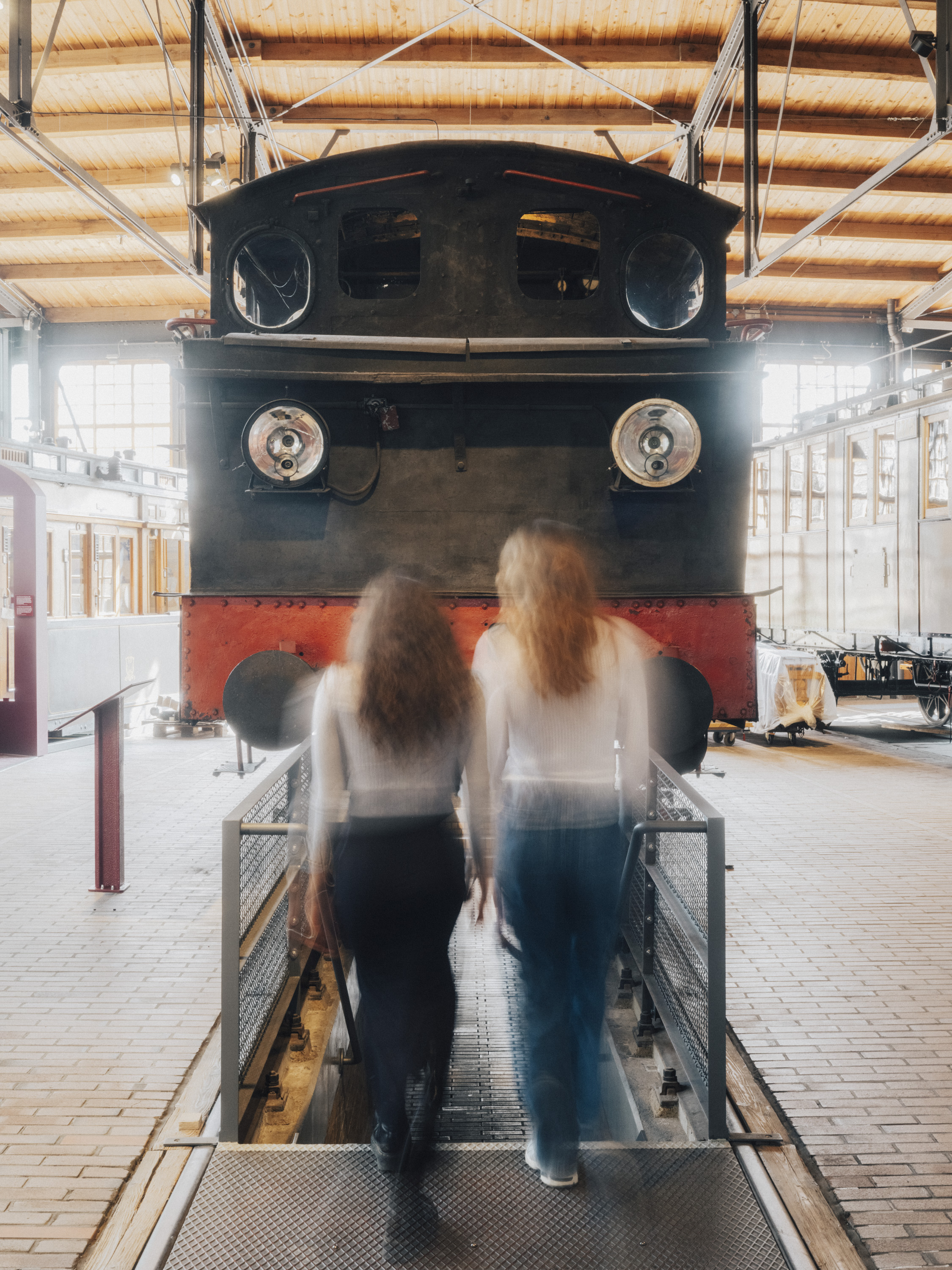Zwei Personen, unscharf fotografiert, vor einer Treppe, die unter eine Lok führt.