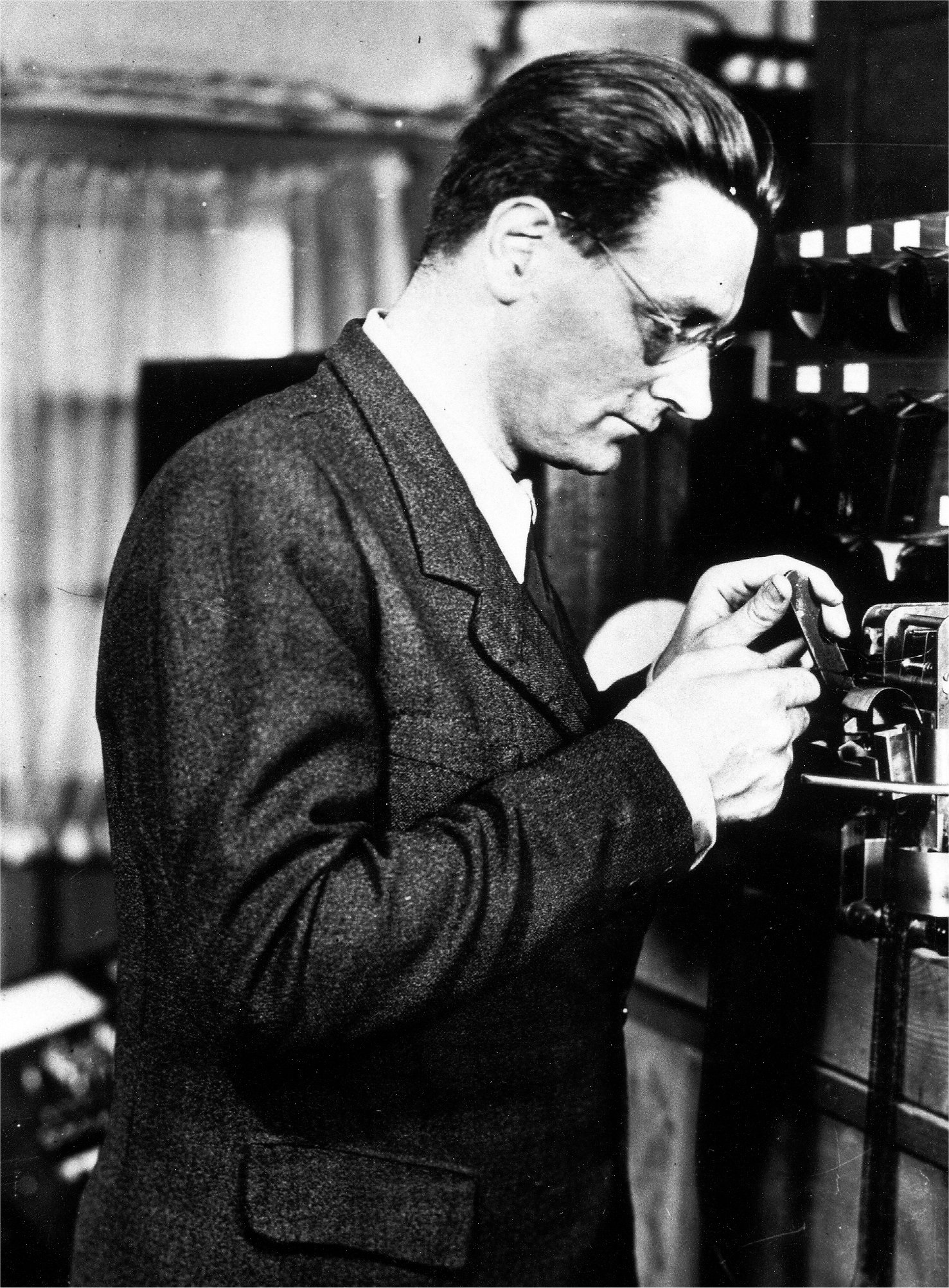 Black-and-white photo: Konrad Zuse in profile, checking a punched tape. 