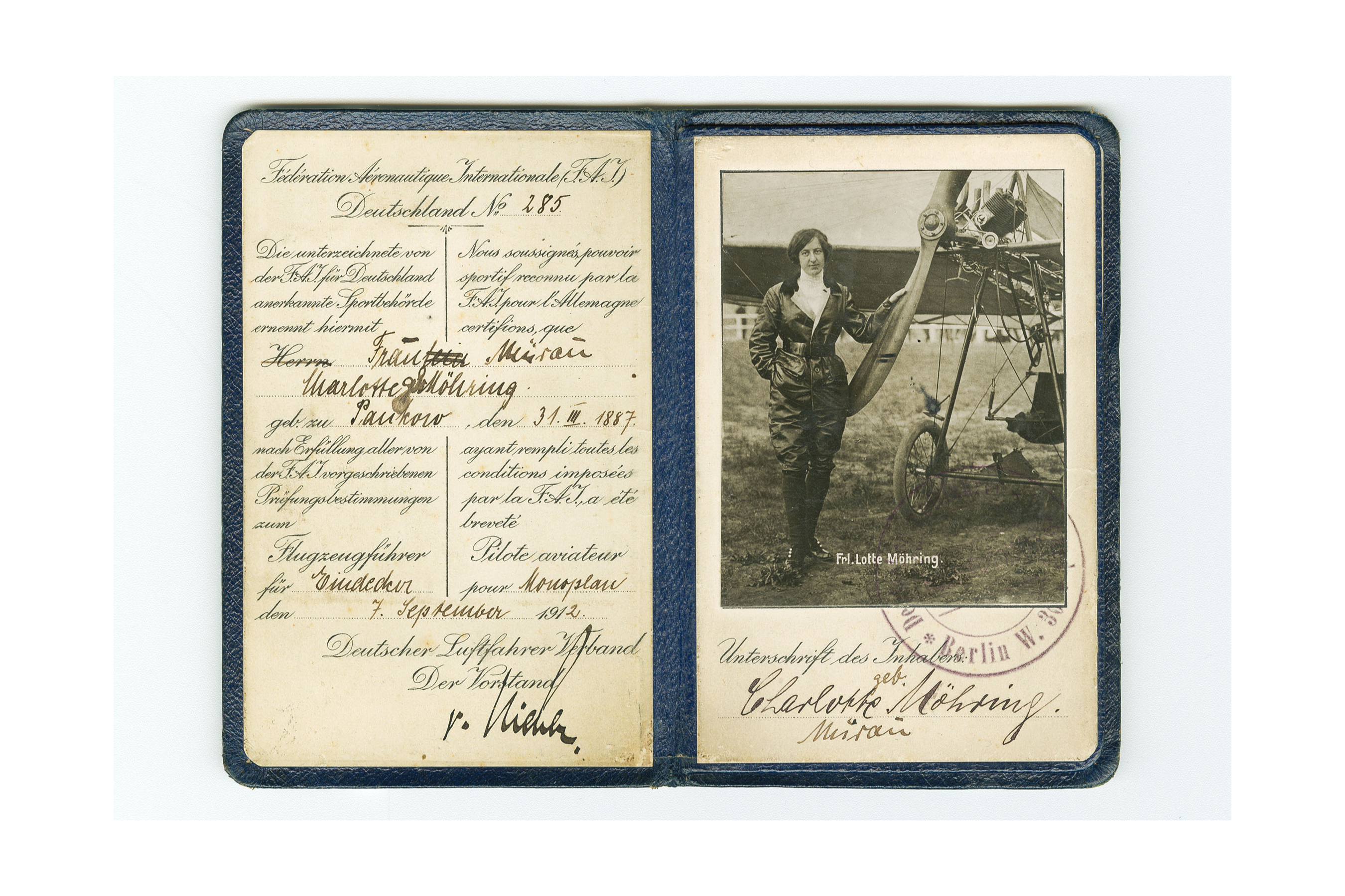 Flugzeugführerschein, aufgeklappt. Die personenbezogenen Daten wurden mit schwarzer Tinte handschriftlich auf der linken Seite eingetragen. Die rechte Seite enthält ein Schwarzweiß-Foto einer Frau vor einem Flugzeug. Unterhalb des Fotos befindet sich die Unterschrift von Frau Charlotte Möhring und ein Stempel.