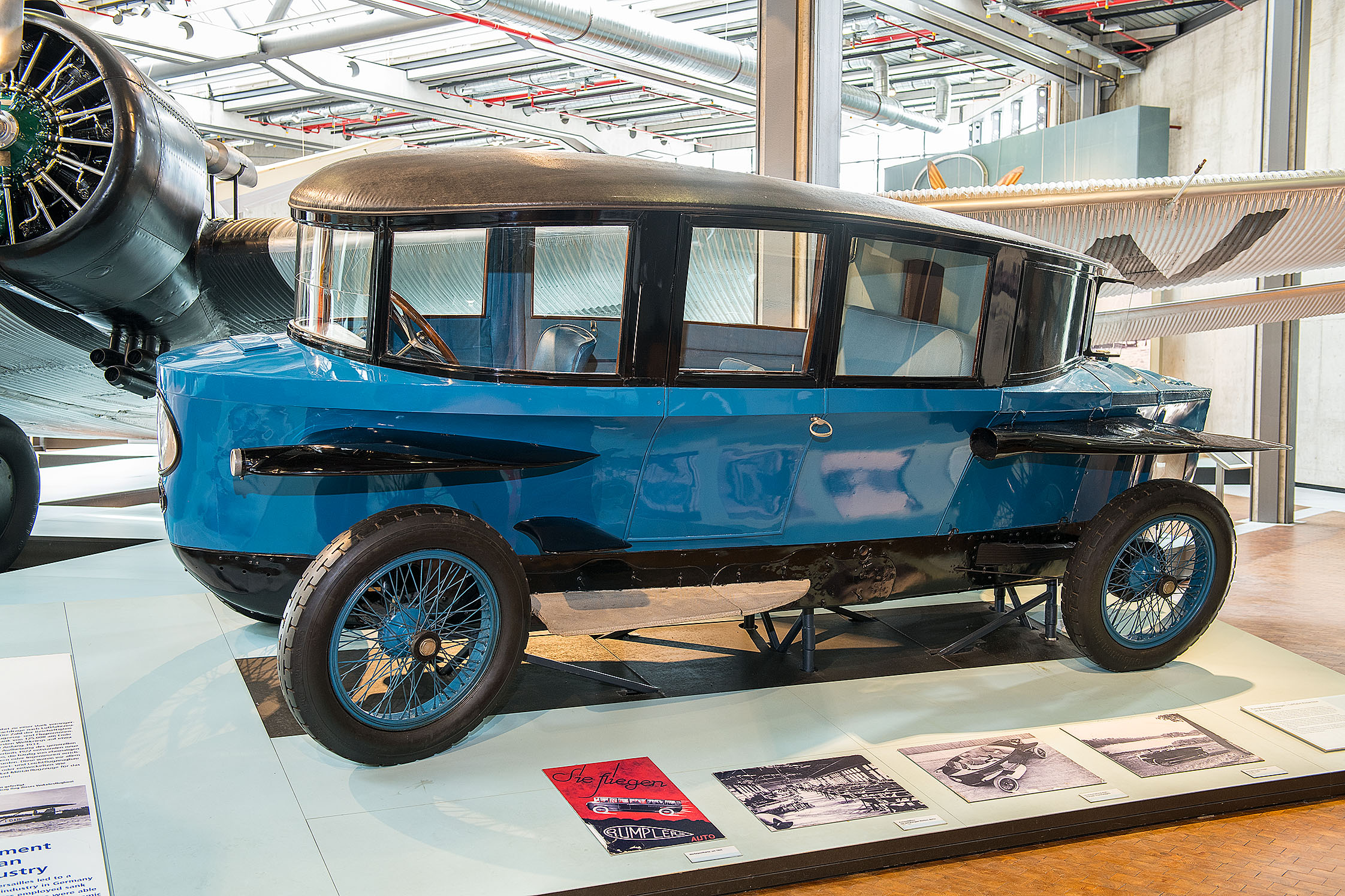 Ein historisches, längliches, blaues Fahrzeug, das durch seine aerodynamische, tropfenähnliche Form auffällt. Das Dach fällt nach hinten ab, Scheinwerfer und Schutzbleche an den Seiten erinnern an Flugzeugflügel.