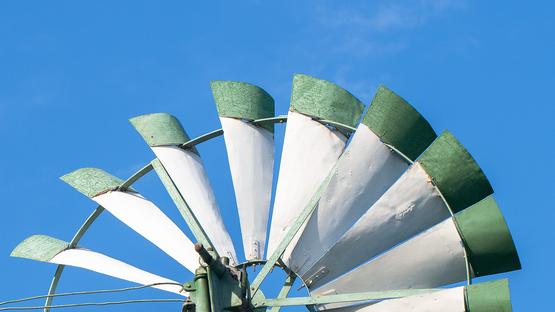 Die obere Hälfte eines Windrads mit grünen Spitzen vor blauem Himmel