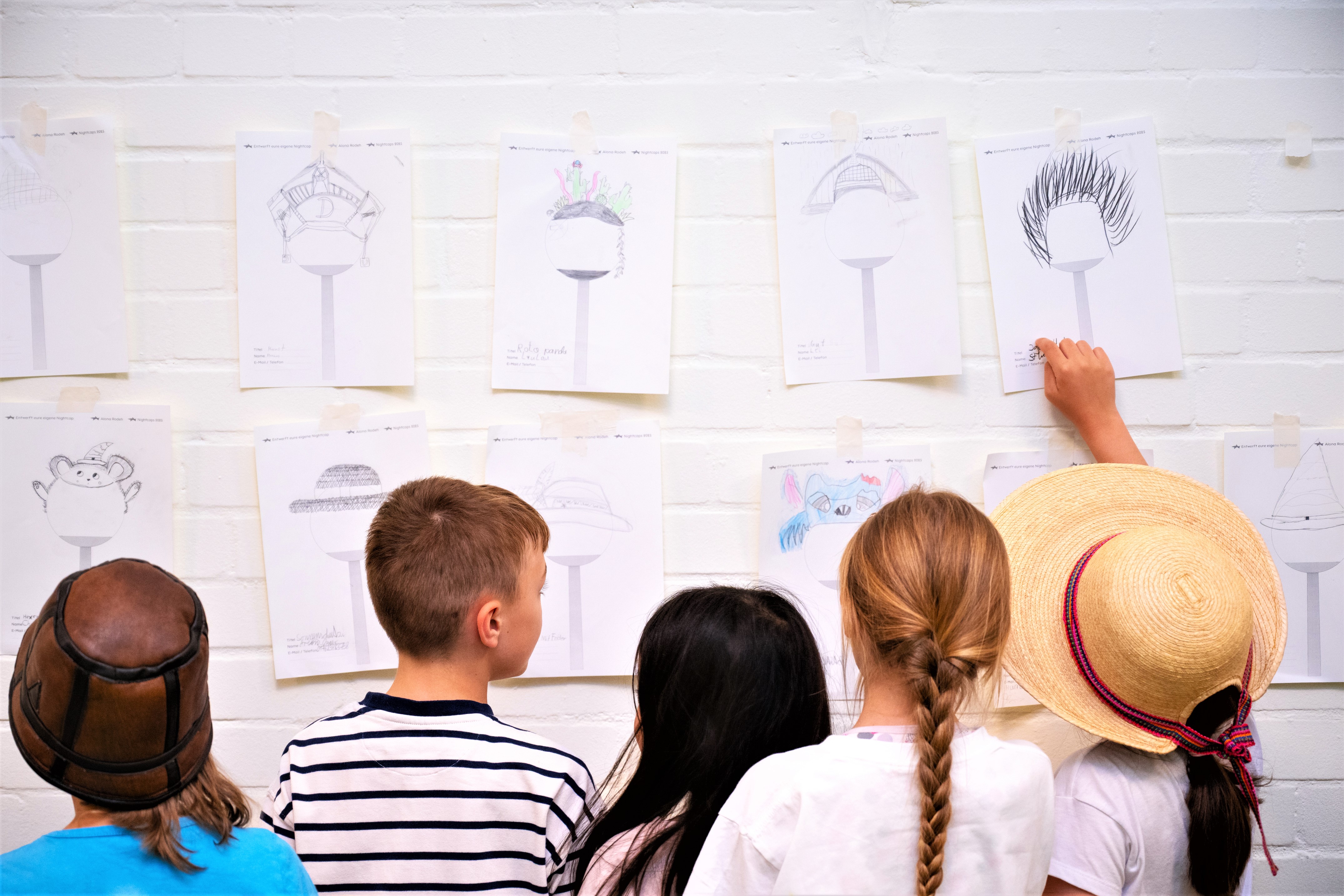 Eine Gruppe Kinder steht vor einer Wand mit Skizzen für Straßenlaterenen die nach oben abstrahlendes Licht abschirmen.