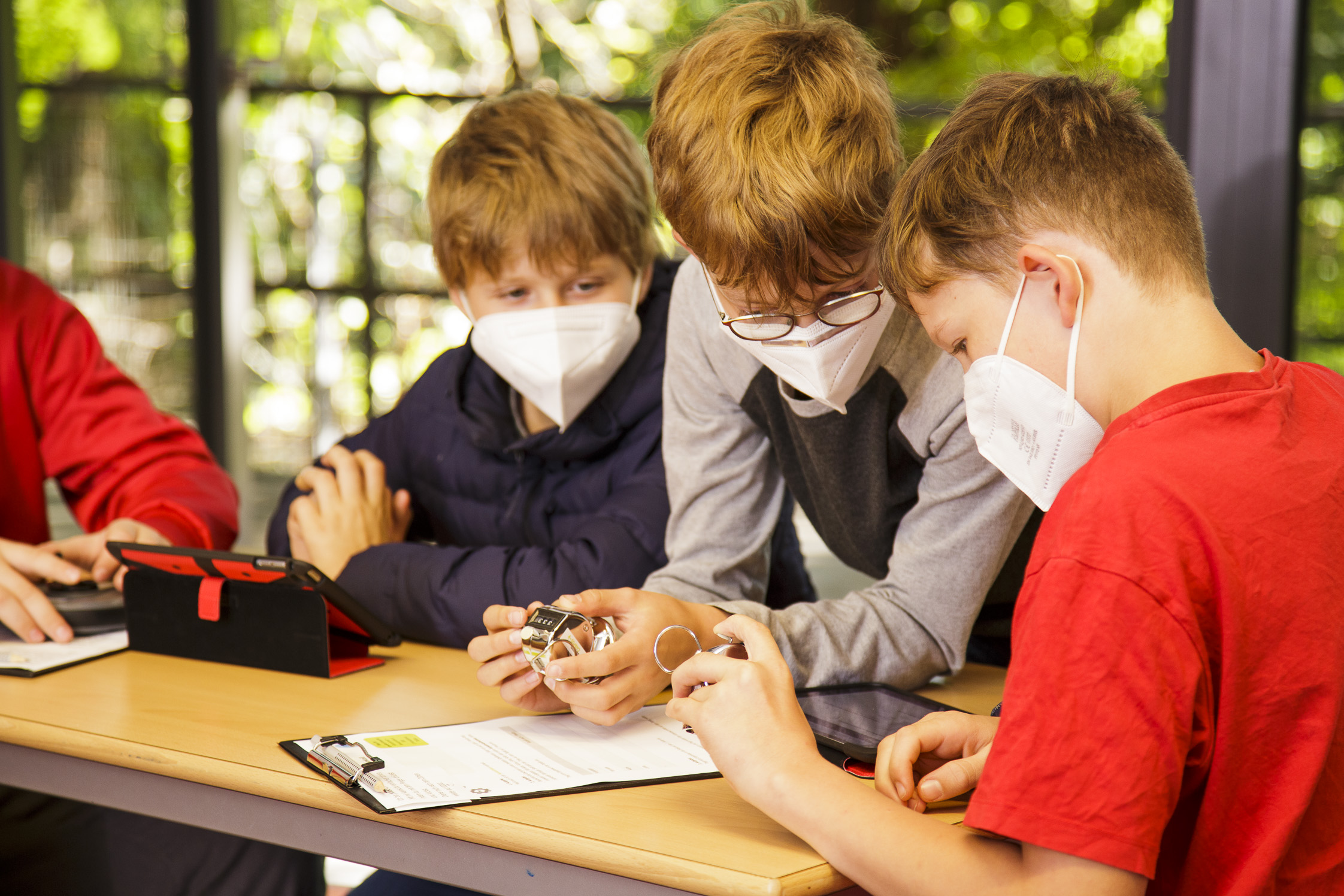 Drei Jungen sitzen an einem Schreibtisch und beugen sich über Notizen. Ein Junge hält ein Messgerät in der hand, ein anderer trägt Messergebnisse in einen Auswertungsbogen ein.