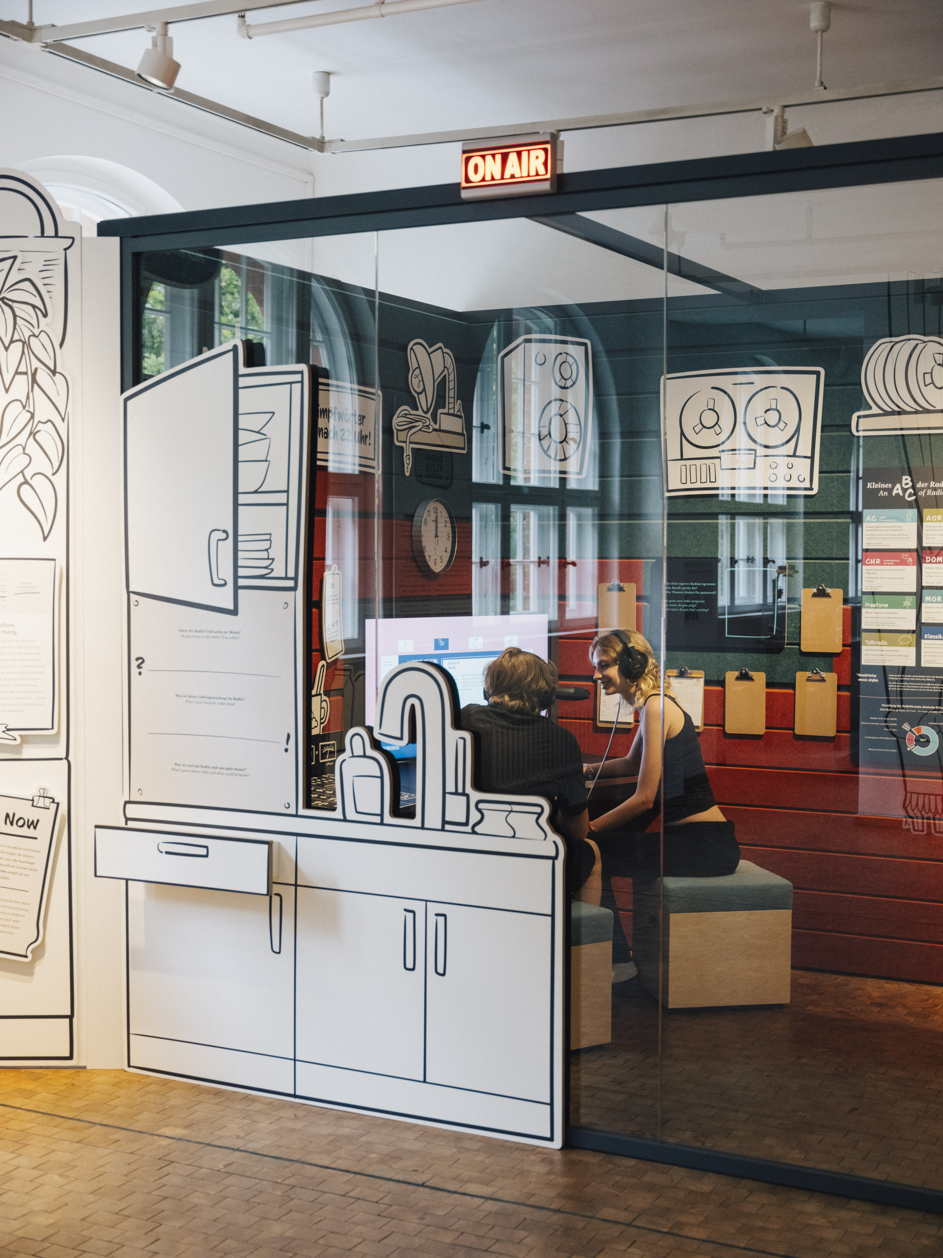 Blick in das gläserne Studio im Ausstellungsbereich "Radio Gleisdreieck". Im Studio sind zwei Personen zu erkennen. Über dem Eingang zum Studio leuchtet der Schriftzug "On Air".