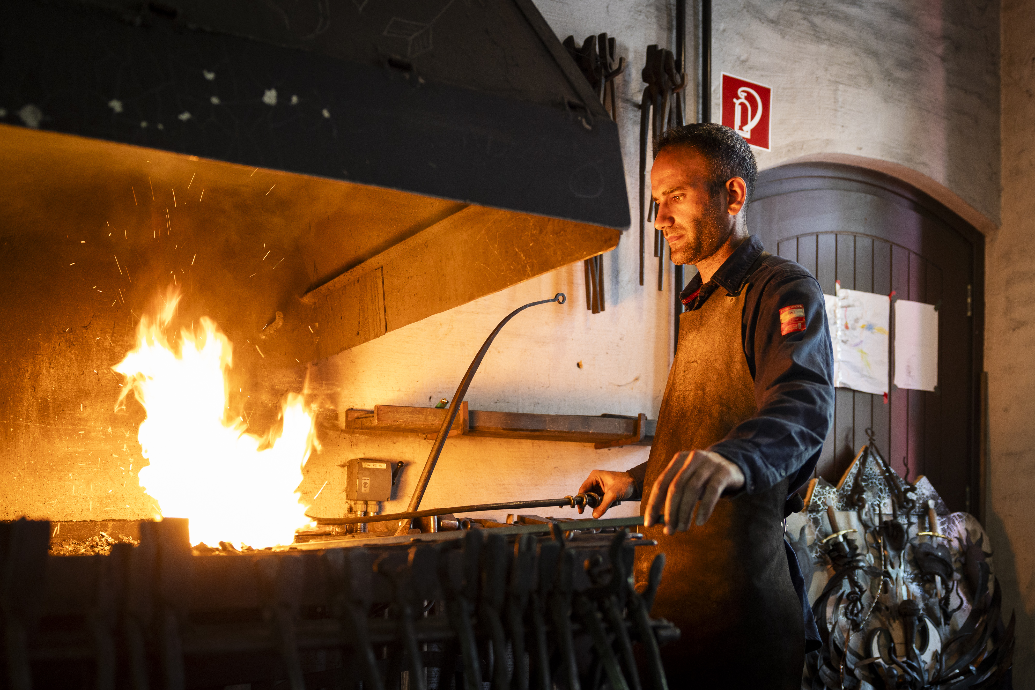 Ein Schmied hält ein Eisenstab in ein offenes Feuer.