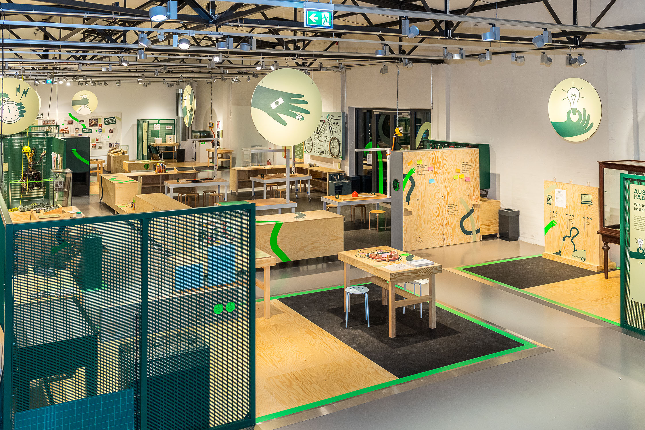 A view of the "Repair!" exhibition area, with its light-colored wooden furniture, workbenches, and graphic icons that help visitors find their way around the exhibition space.