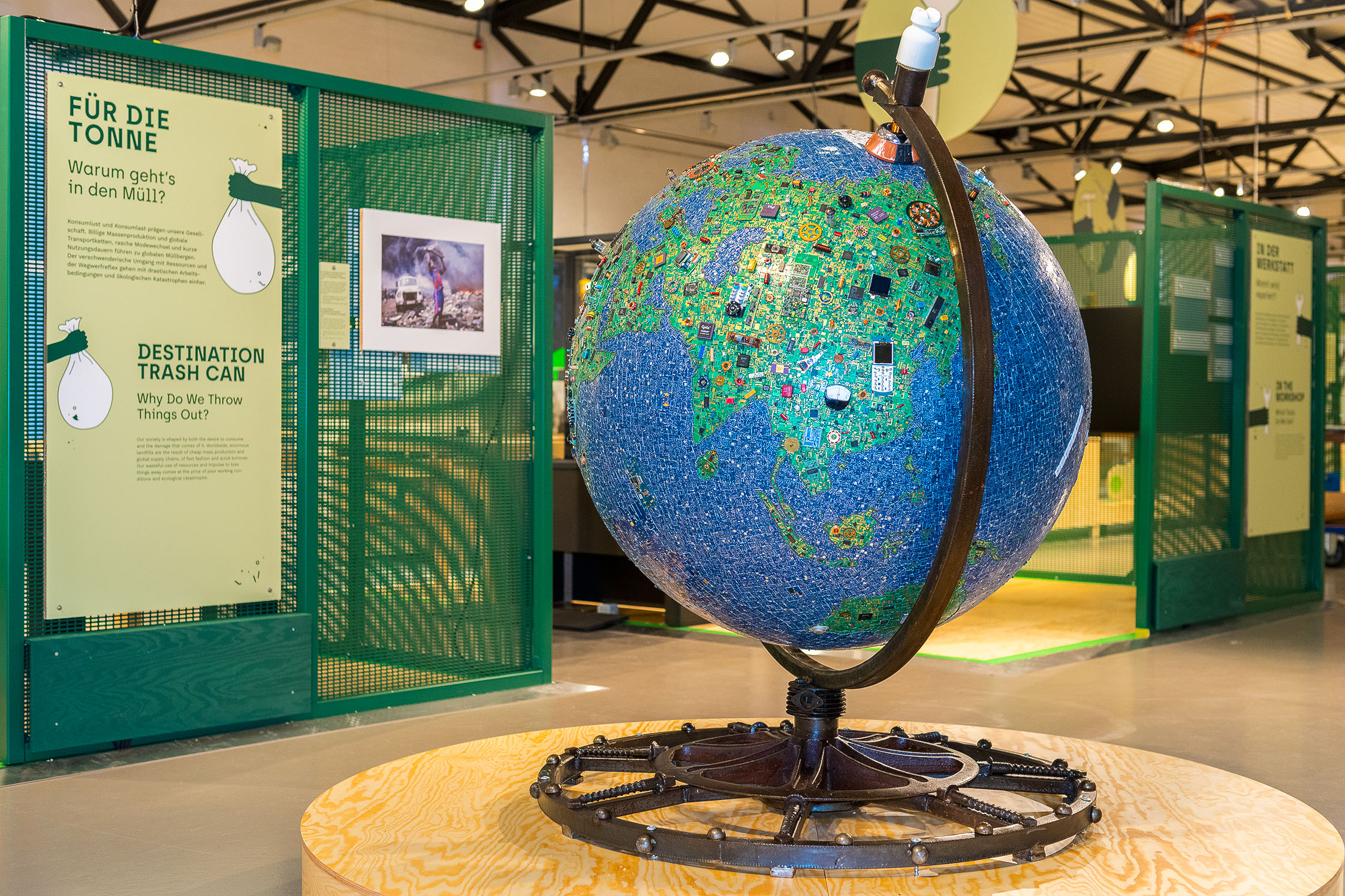 A large globe is on display in the exhibition’s entrance area. Its surface depicts the globe as a mosaic of electronic waste: the oceans are made of small blue circuit board pieces, forests of green circuit boards, and mountains of brown cables. 