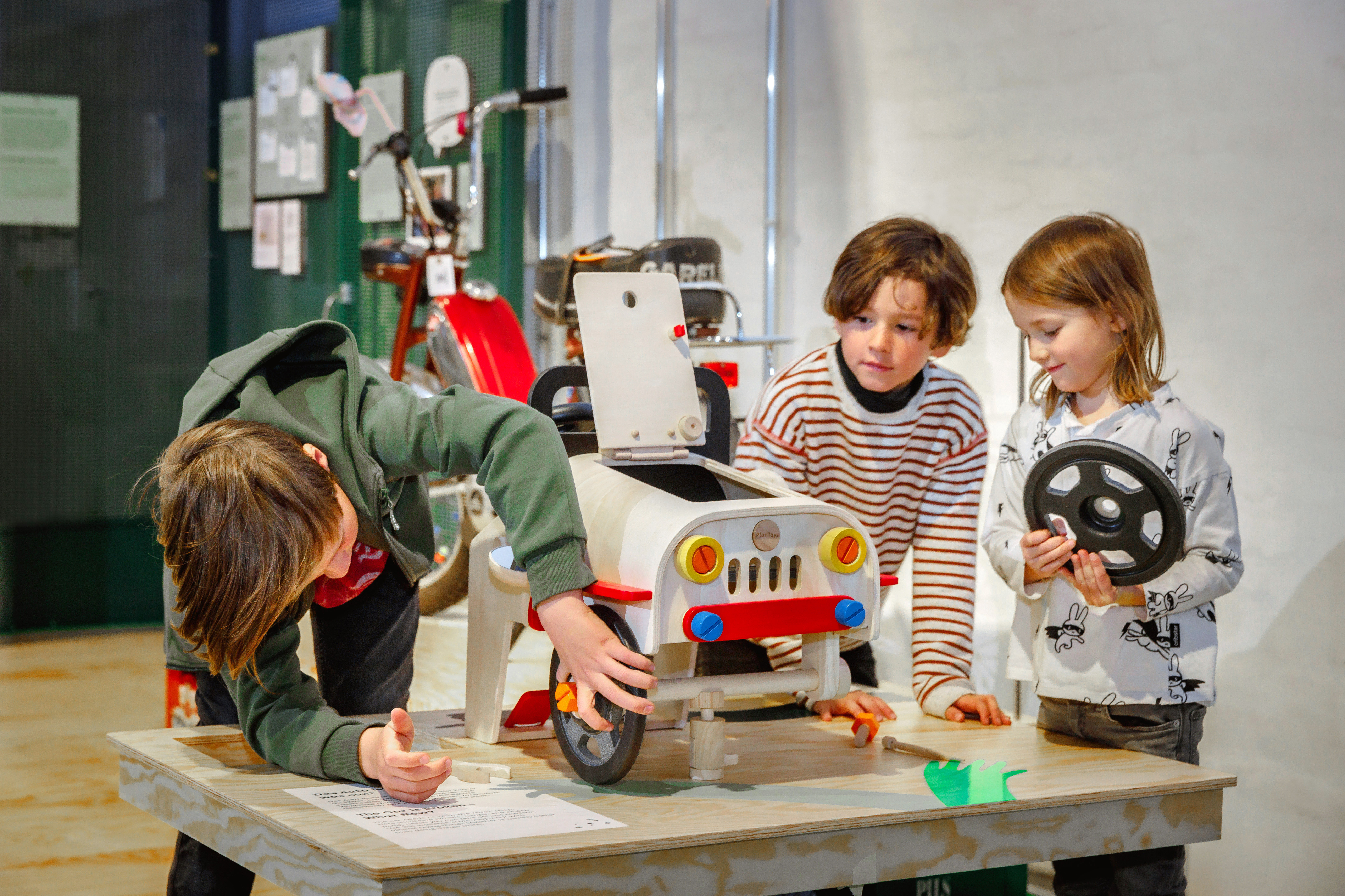 Three children are working together to assemble a colorful wooden car that is sitting on a table.