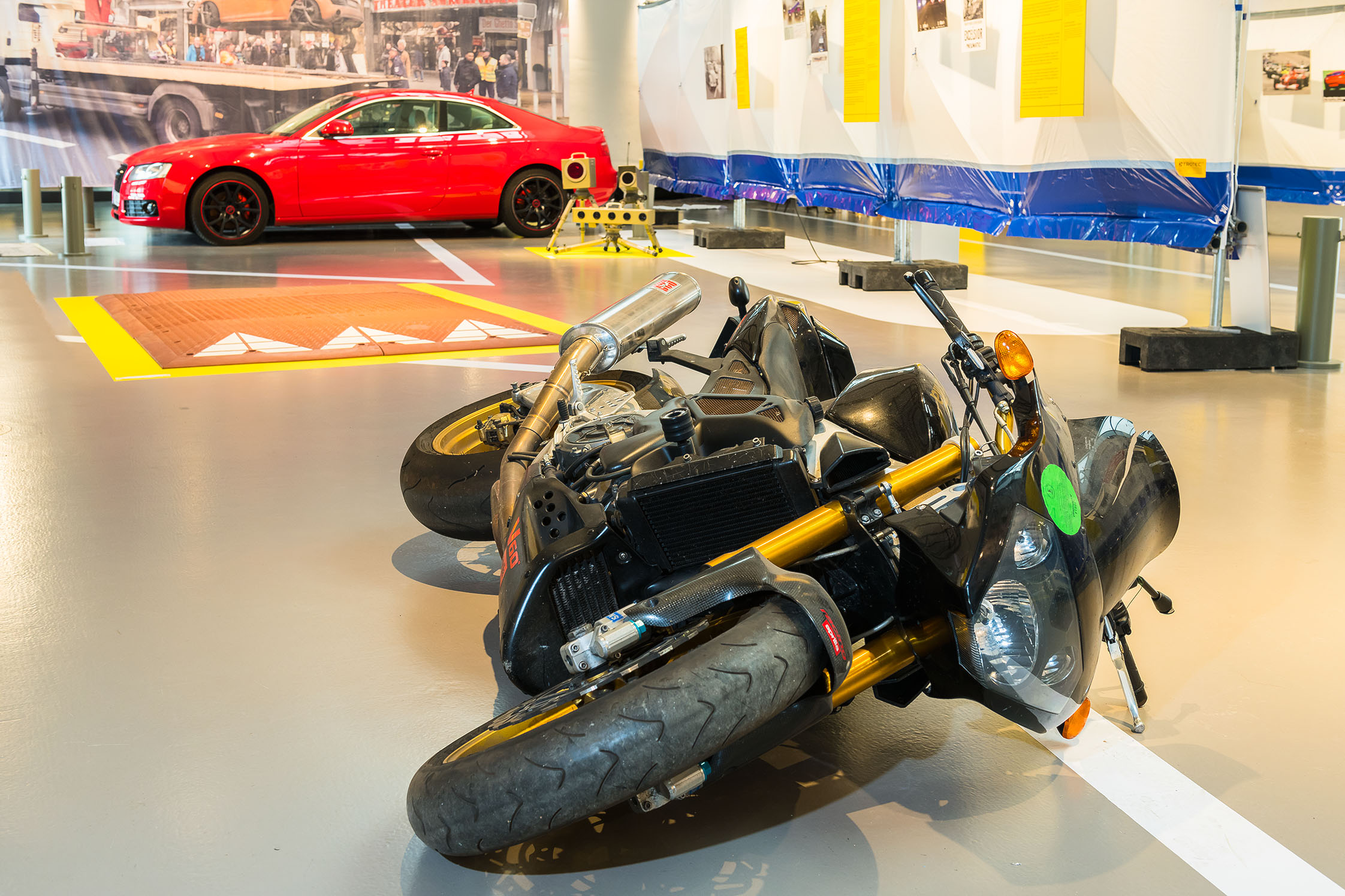 A black motorcycle is lying on the ground; a red car can be seen in the background.