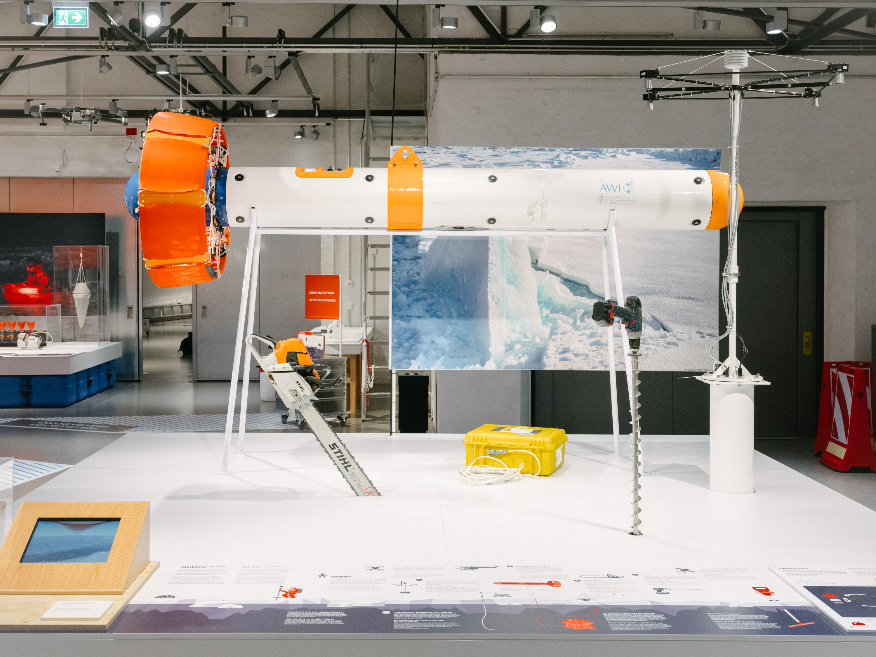 Several pieces of equipment are on display on a platform: a large probe, a chainsaw, a large drill, and other measuring instruments. 