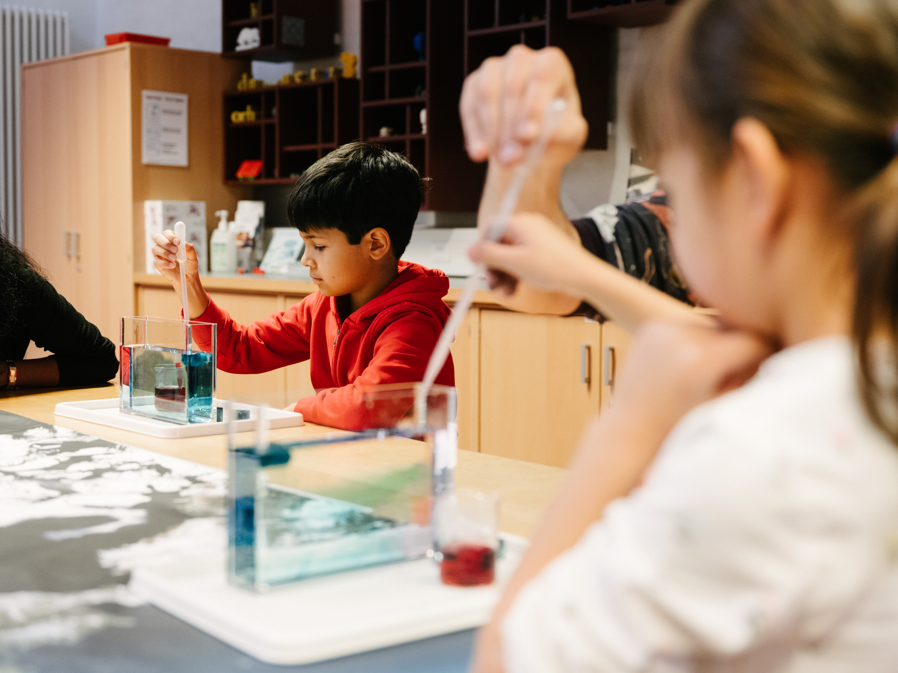 Two children are experimenting with water, ice, and pipettes at a table.