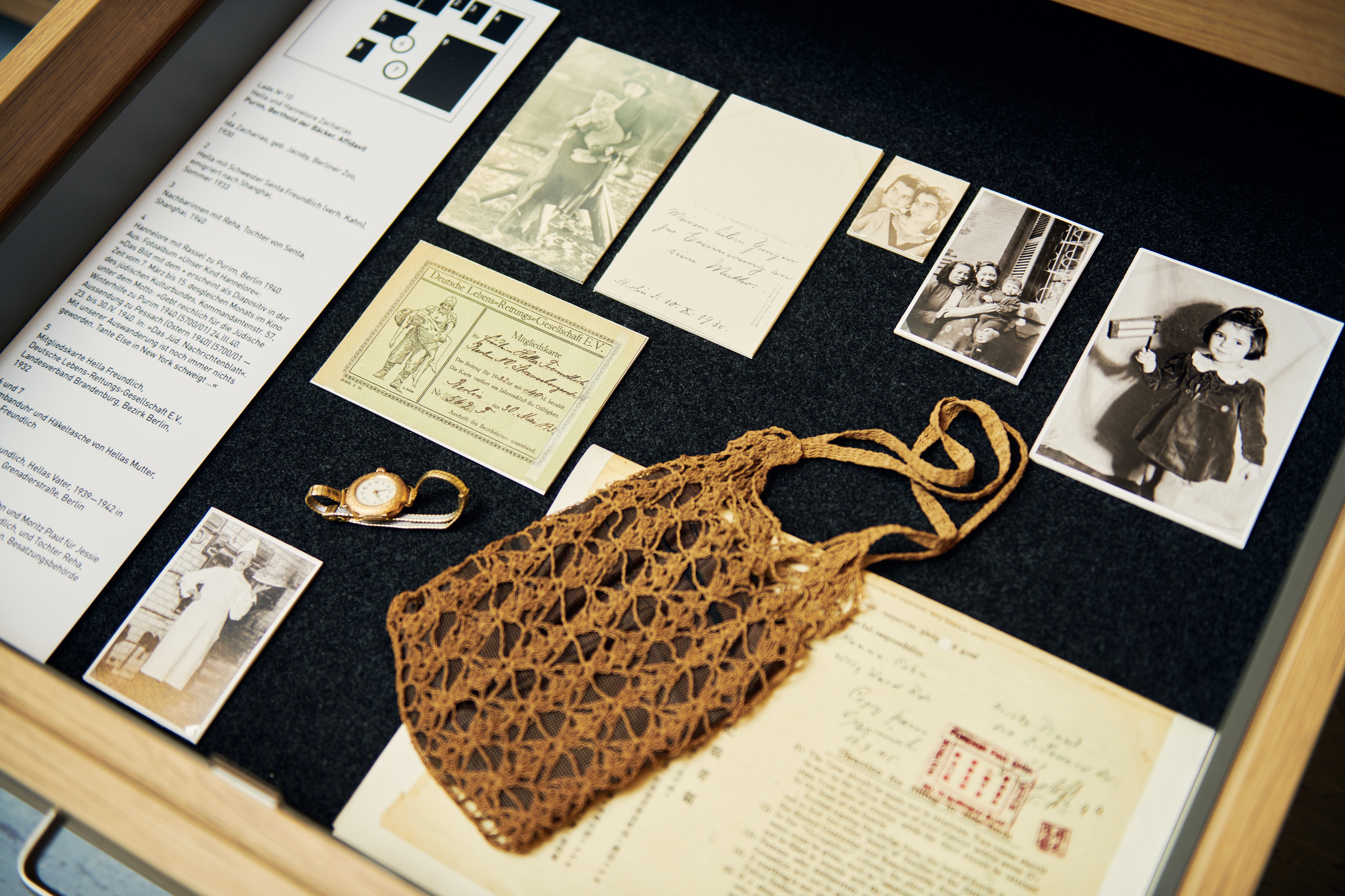 A view inside an open drawer. You can see family photos, as well as a wristwatch and a crocheted women's handbag.