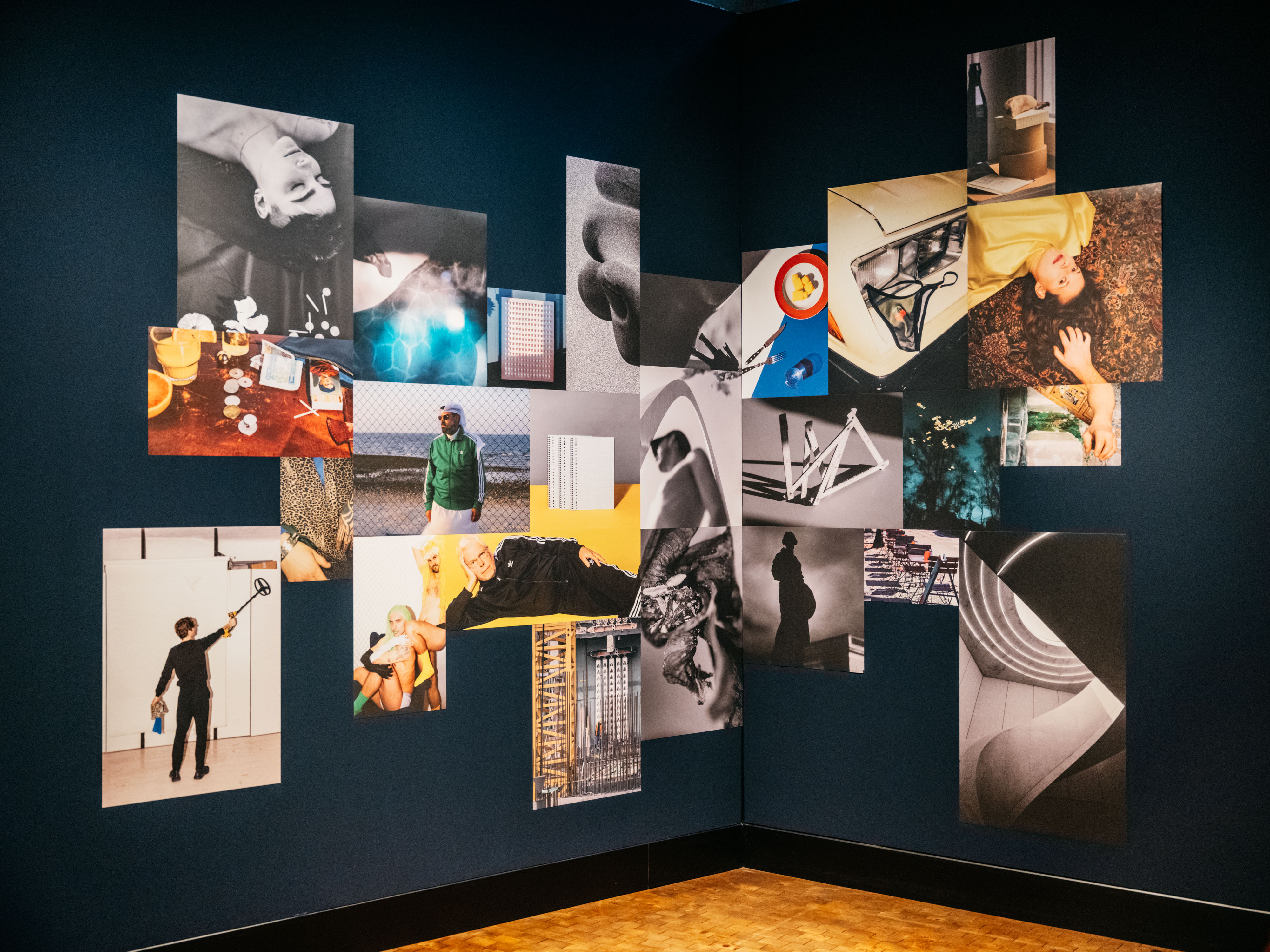 Ein Mosaik aus Fotos hängt an einer dunkelblauen Wand. Auf den einzelnen Fotos sind Bezüge untereinander erkennbar.