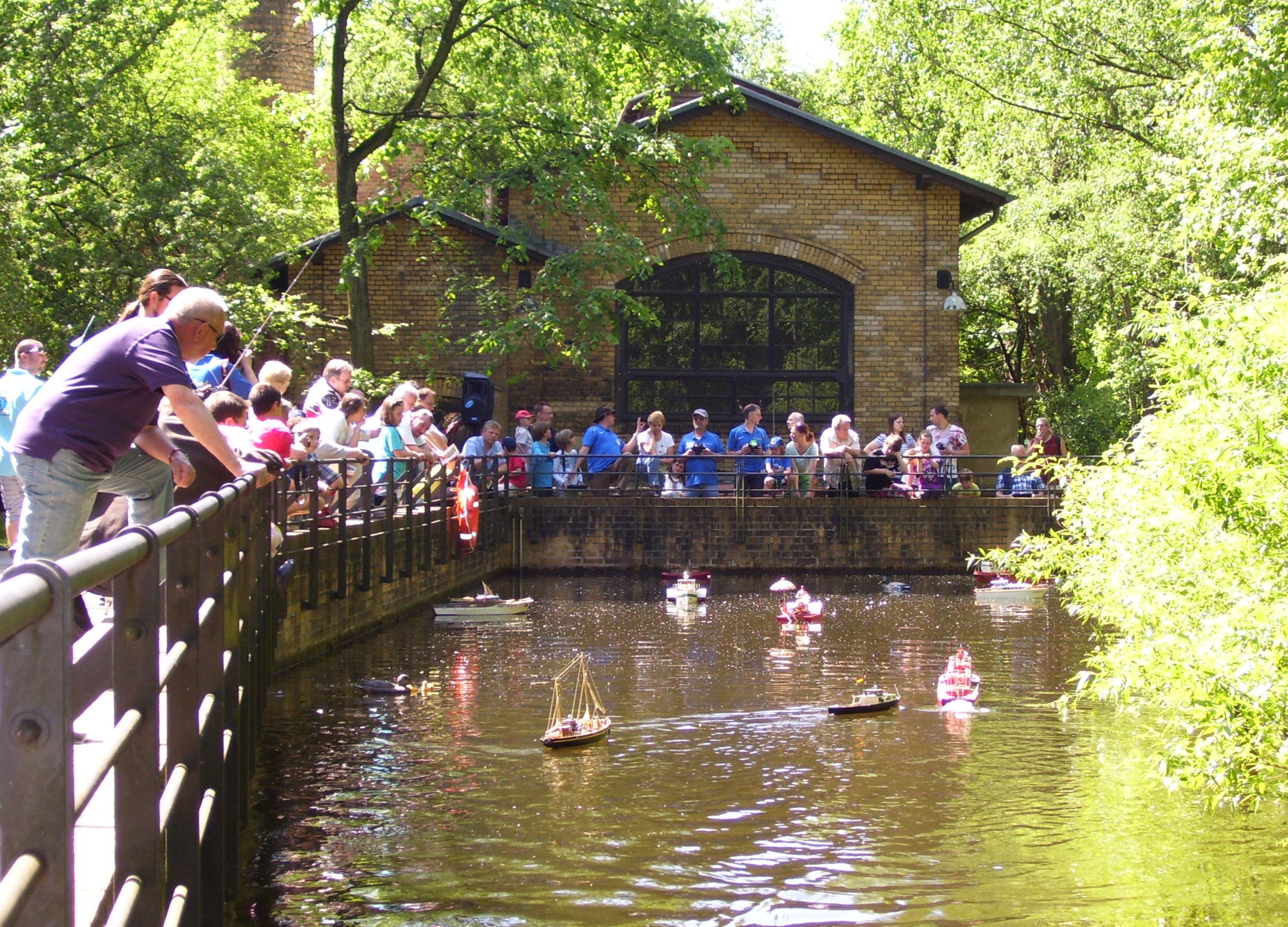 Besucherinnen und Besucher schauen auf den Museumsteich im Park, auf dem kleine Modellschiffe hin und her fahren.