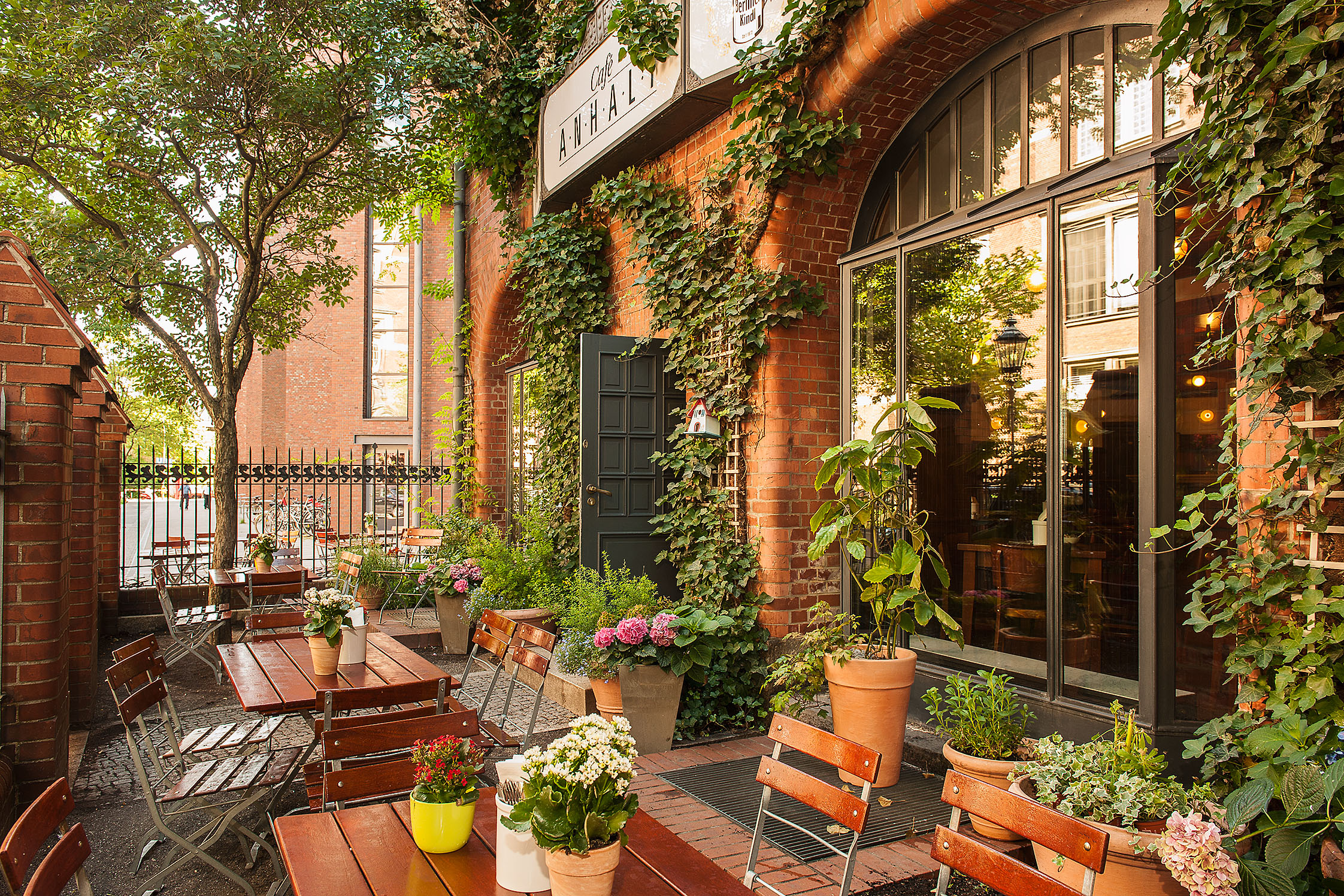 A view of a restaurant's terrace, adorned with greenery and featuring invitingly decorated wooden tables and chairs. 